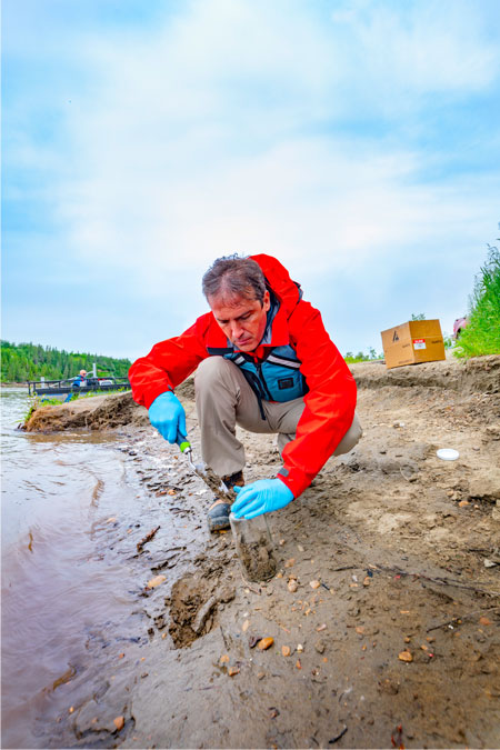 Photo of a scientist collecting samples from a river shoreline